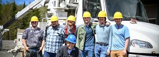Graduating class of Vermont broadband technicians in hard hats standing in front of a bucket truck