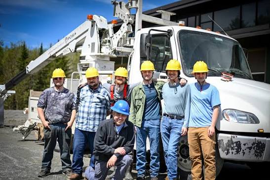 Graduating class of Vermont broadband technicians in hard hats standing in front of a bucket truck